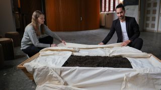 Archivbild: Pablo Metz und Olga Perov falten ein Tuch in einem Sarg mit Erde bei einem Pressegespräch zu der neuen Bestattungsform "Reerdigung". (Quelle: dpa/Charisius)