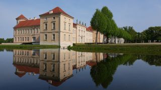 Archivbild: Die Parkseite von Schloss Rheinsberg mit dem Kurt Tucholsky Literaturmuseum spiegelt sich in dem vom Grienericksee gespeisten Wasser des Schlossgrabens. (Quelle: dpa/Stache)