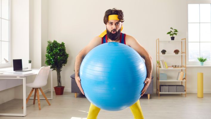 Ein Mann in Sportoutfit hebt einen Gymnastikball hoch. (Quelle: Colourbox)