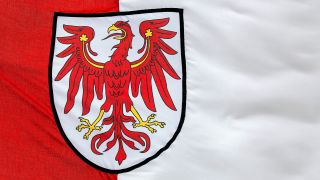 Symbolbild: Ausschnitt der Landesflagge Brandenburgs mit Landeswappen. (Quelle: dpa/Torsten Sukrow)