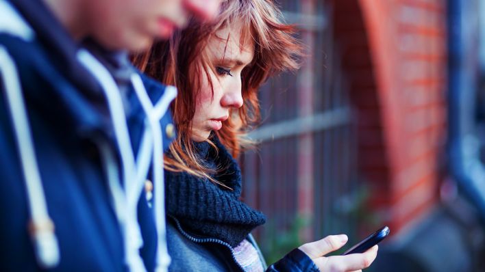 Symbolbild: Eine junge Frau guckt auf das Bildschirm ihres Smartphones. (Quelle: dpa/Westend61)