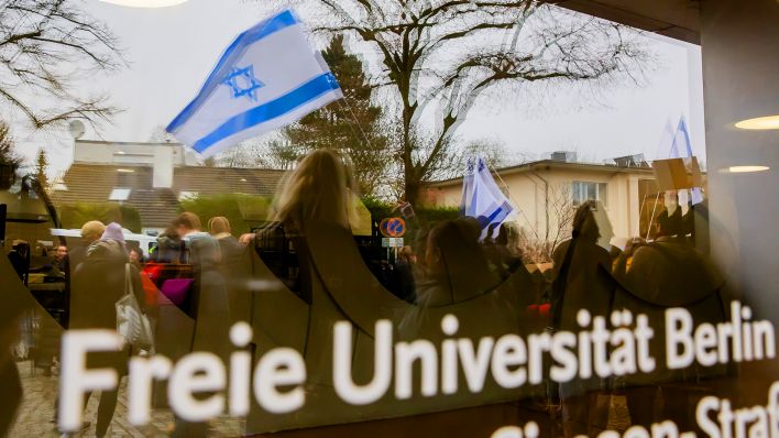 Symbolbild: Eine Israel-Flagge spiegelt sich bei einem stillen Protest einer Initiative für die Sicherheit jüdischer Studierender in einer Scheibe der Freien Universität Berlin. (Quelle: dpa/Christoph Soeder)