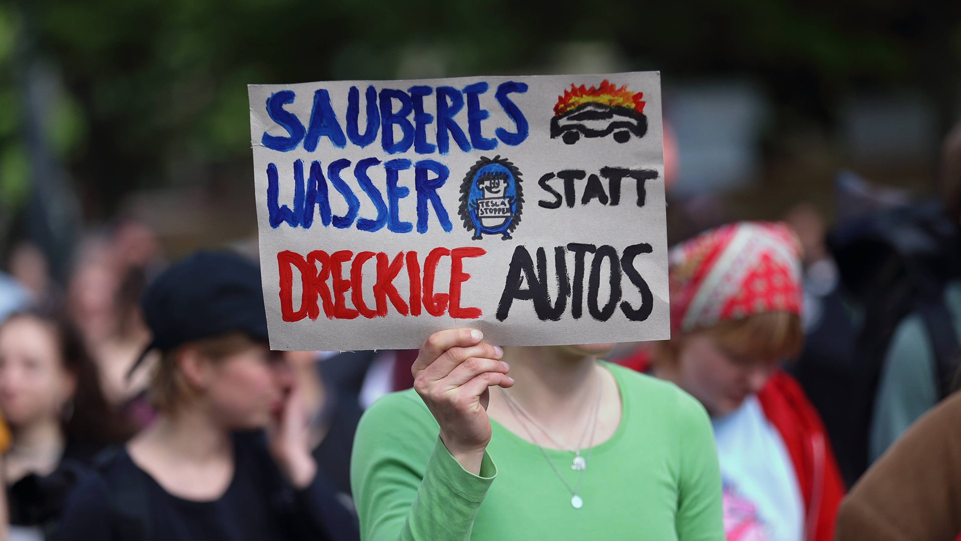 Eine Demonstrantin läuft am 08.052024 in Potsdam mit einem Schild "Sauberes Wasser statt dreckige Autos" auf einer Demonstration gegen die geplante Erweiterung der Tesla Gigafactory in Grünheide (Mark). (Quelle: Imago Images/Martin Müller)