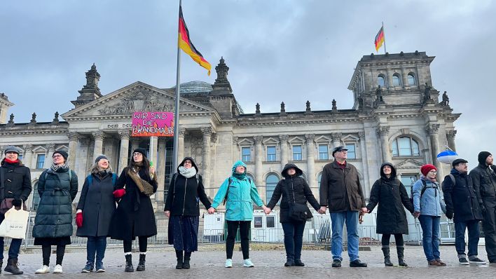 "Wir sind die Brandmauer" steht vor einer Menschenkette vor dem Reichstagsgebäude am 03.02.2024 auf einem Schild. (Quelle: rbb/Grit Lieder)