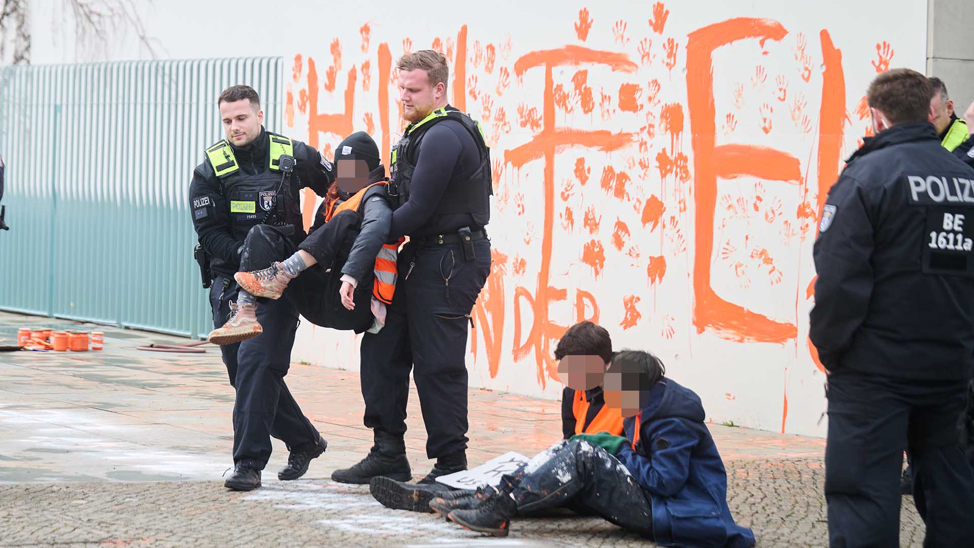"Hilfe! Eure Kinder" steht mit der Farbe Orange ans Kanzleramt geschmiert, während eine Klimaaktivistin der letzten Generation von Polizisten weggetragen wird. (Quelle: dpa/Riedl)