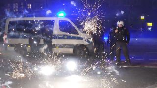 Symbolbild: Polizeibeamte stehen in der Siolvesternacht hinter explodierendem Feuerwerk. (Quelle: dpa/TNN)