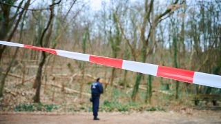 28.02.2024, Berlin: Ein Polizeibeamter steht in einem Waldgebiet im Volkspark Prenzlauer Berg hinter einem Absperrband. (Quelle: dpa/Annette Riedl)