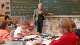 Symbolbild: Lehrerin steht im Klassenraum (Bild: imago images/Sven Simon)