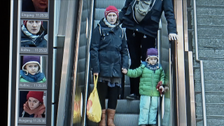 Mutter und Kind auf der Rolltreppe, ihre Gesichter werden durch ein Gesichtserkennungsprogramm analysiert.