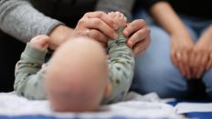 Symbolbild:Ein Vater hält während eines Infant Handling Kurses die Füße seines Kindes, während die Mutter daneben sitzt.(Quelle:picture alliance/dpa/M.Murat)