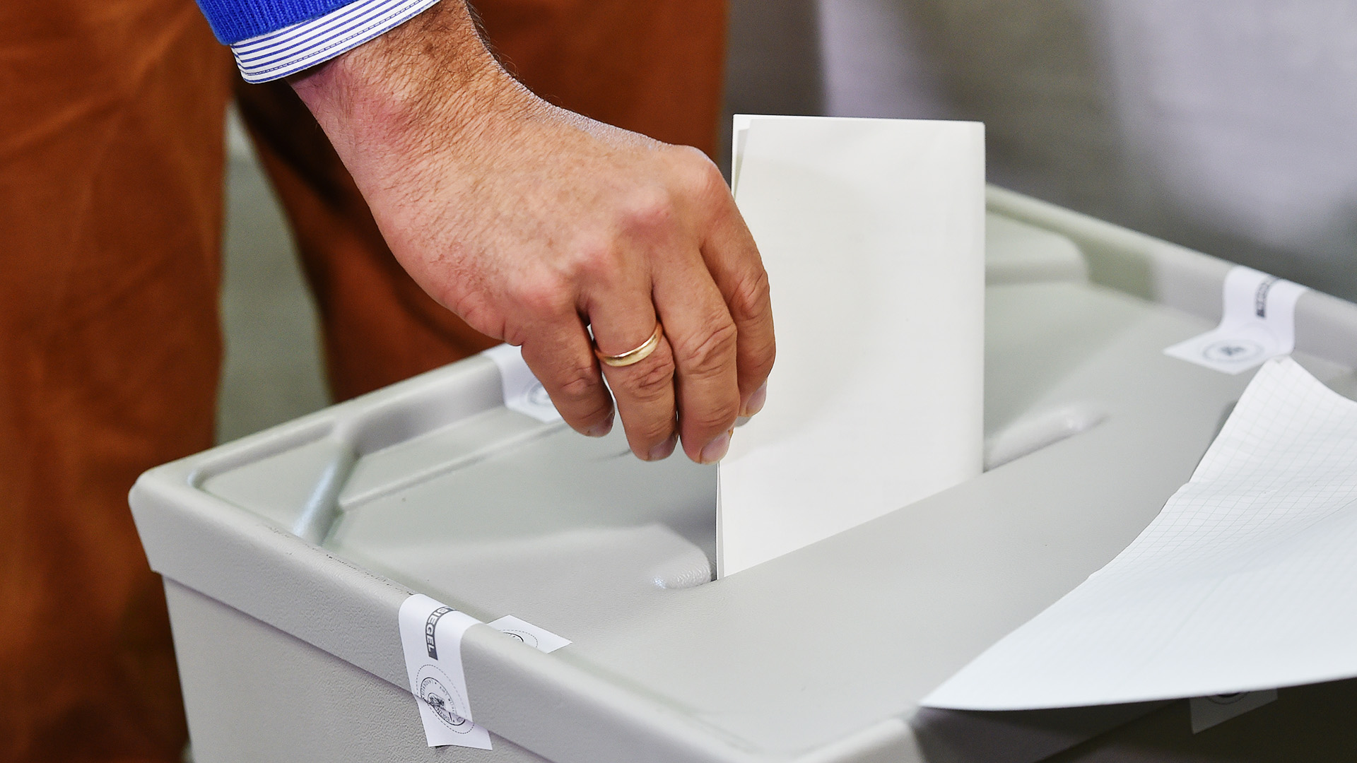 Eine Hand wirft einen gefalteten Wahlzettel in den Schlitz einer Wahlurne.