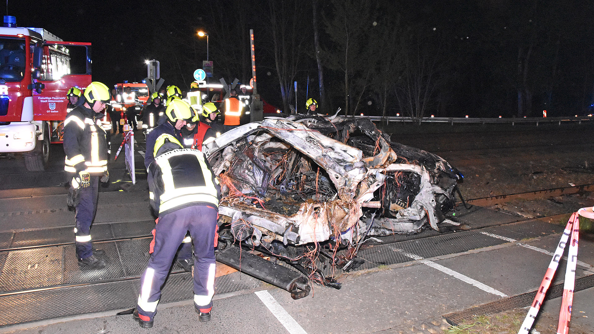 Originalbild: Rettungskräfte stehen am Wrack eines zerstörten Autos nach einem Unfall an einem Bahnübergang am 12.04.2024, Brandenburg, Bestensee.(Quelle: dpa/Christian Sappeck)