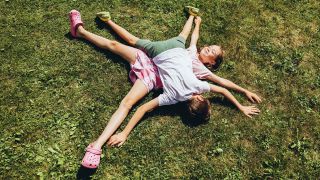 Symbolbild:Zwei Kinder liegen übereinander auf dem Rasen.(Quelle:imago images/Cavan Images)