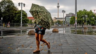 Eine junge Frau versucht, sich vor dem Regen mit einem Schirm zu schützen. (Quelle: dpa-Zentralbild/Britta Pedersen)