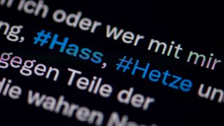Symbolbild: Auf dem Bildschirm eines Smartphones sieht man die Hashtags (#) Hass und Hetze in einem Twitter-Post. (Quelle: dpa/Sommer)