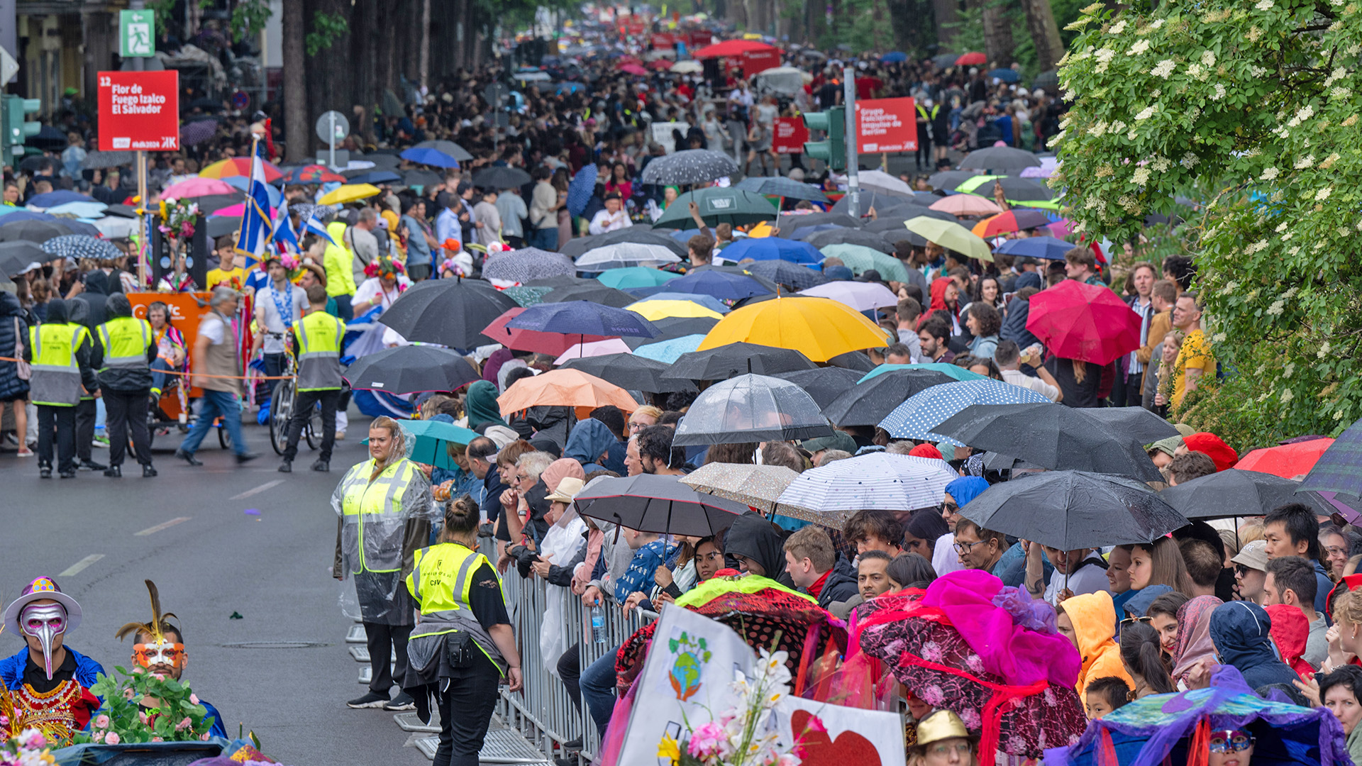 Zuschauer mit Regenschirmen verfolgen am 19.05.2024 bei Regen die Parade zum 26. Karneval der Kulturen. (Quelle: dpa-Bildfunk/Monika Skolimowska)
