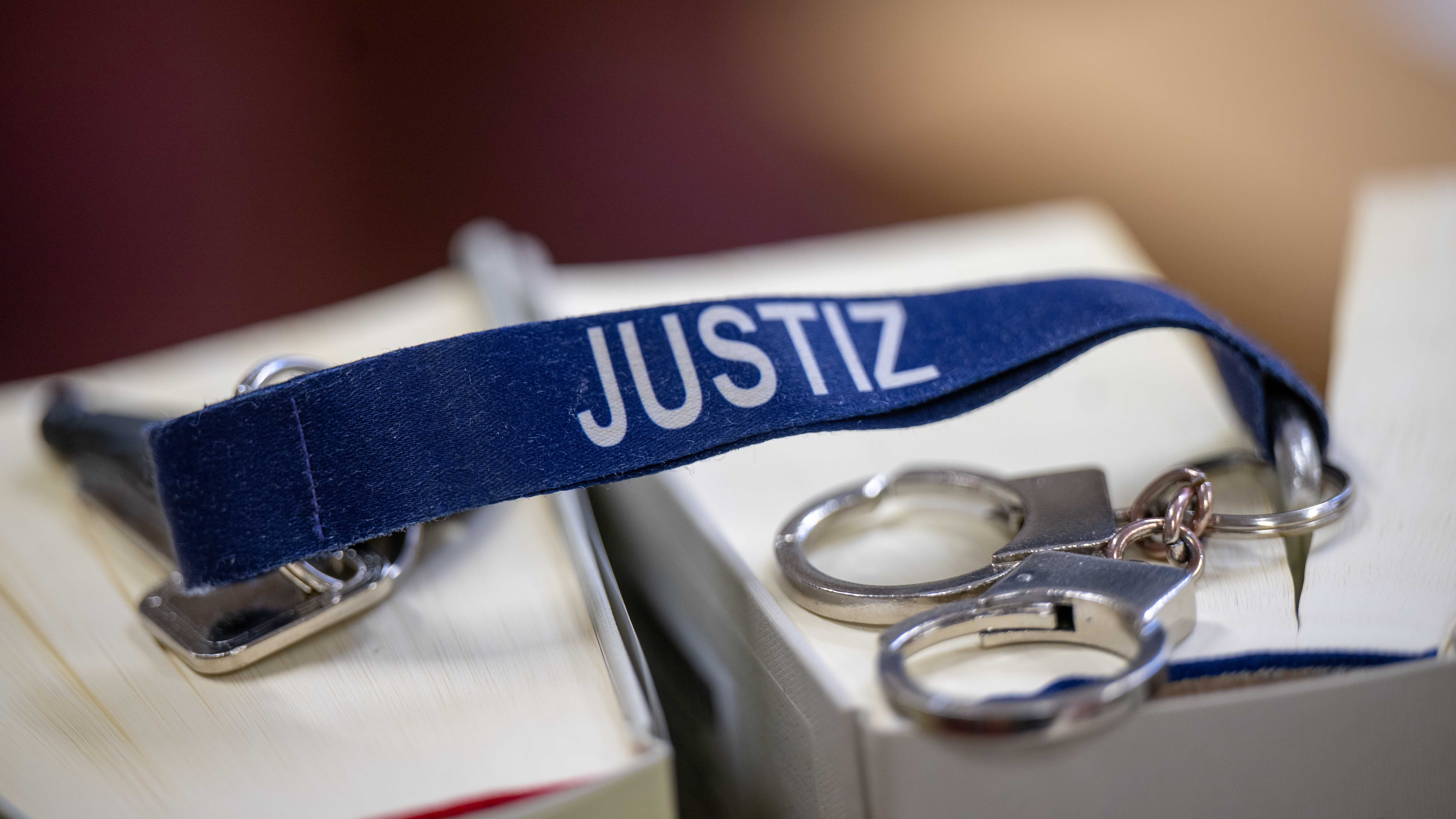 Ein Schlüsselanhänger mit dem Wort «Justiz» und Mini-Handschellen liegen auf zwei Gesetzbüchern im Büro einer Richterin im Kriminalgericht Moabit. (Bild: dpa-news/Monika Skolimowska)