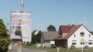 Häuser, Wahlplakat zu erneuerbaren Energien, Windräder im Hintergrund.