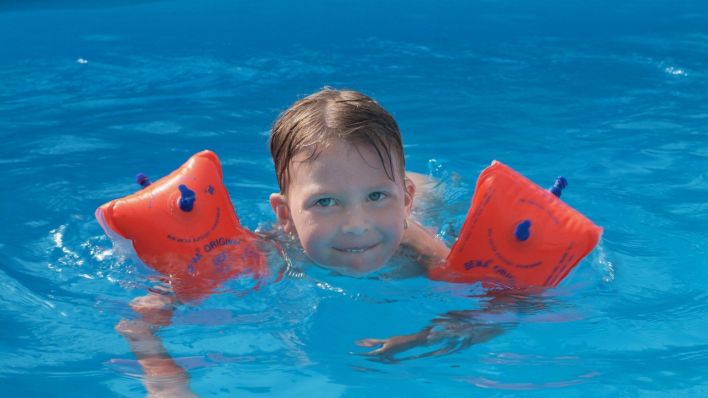 Junge mit Schwimmflügeln im Schwimmbad