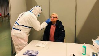 Mann wird im Testzentrum Frankfurt von Person in weißem Schutzanzug getestet