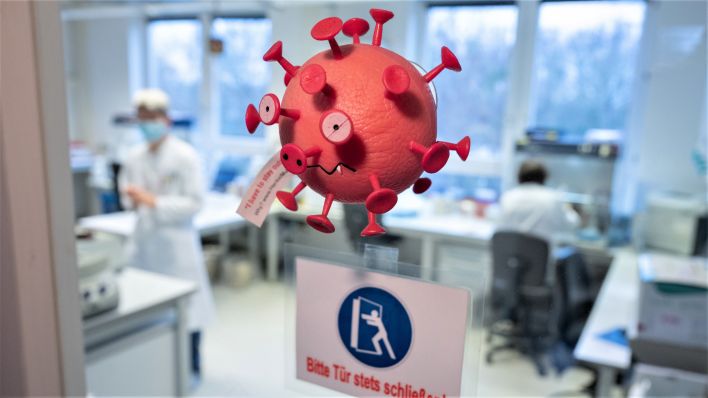 Eine Figur in Optik eines Virus hängt an der Tür vom PCR-Labor . (Quelle: Julian Stratenschulte/dpa)