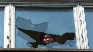 Ein Mann blickt am Tag nach den ausländerfeindlichen Übergriffen durch die eingeworfene Scheibe eines Wohnheims (Archivfoto: dpa/Weißflog)