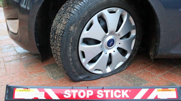 Ein Stop-Stick liegt vor einem Auto mit plattem Reifen (Symbolfoto: dpa/picture alliance /rtn - radio tele nord)