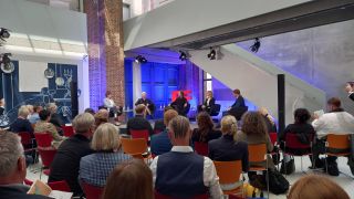 Im Dieselkraftwerk in Cottbus sitzen Menschen zur Pressekonferenz zusammen, in der das Programm des Lausitzfestivals 2022 vorgestellt wird