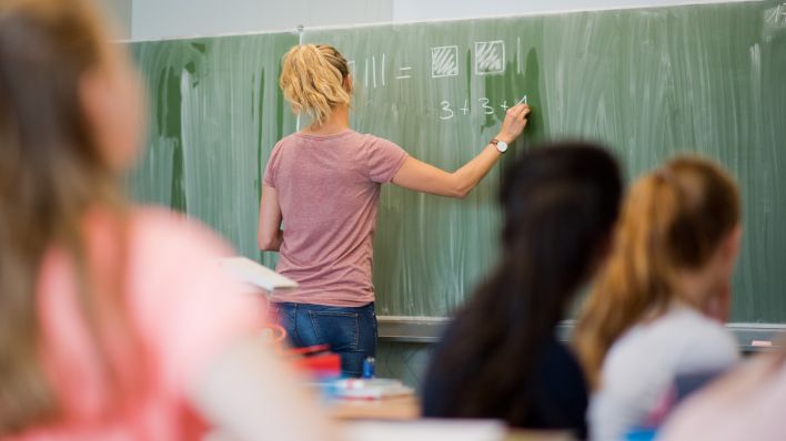 Eine junge Lehrerin schreibt an eine Schultafel im Mathematikunterricht an einer Schule (Foto: dpa/Stratenschulte)