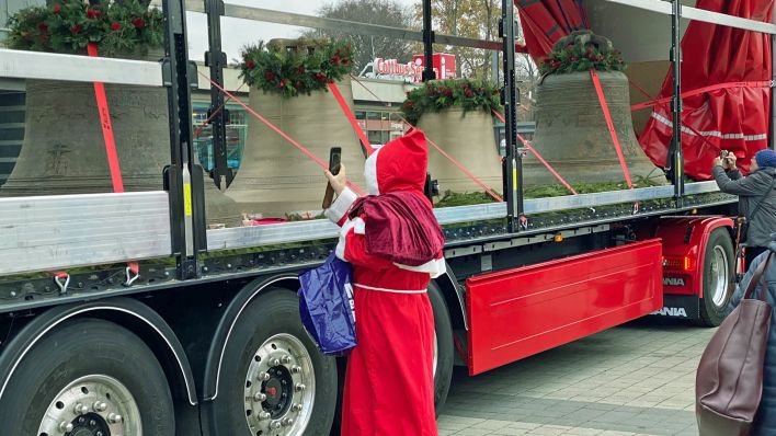 Ein Weihnachtsmann fotografiert die neuen und restaurierten Glocken, die auf einem Lkw-Anhänger stehen (Foto: rbb/Engelmann)