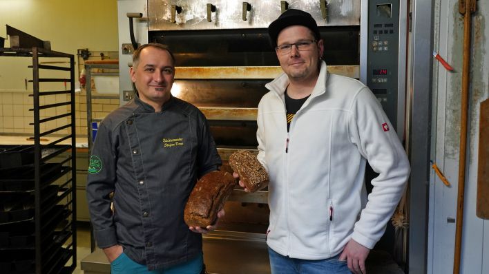 Bäckermeister Stefan Dorn und Brotsommelier Paul Müller vor dem Backofen mit jeweils einem ihrer Brote in der Hand.