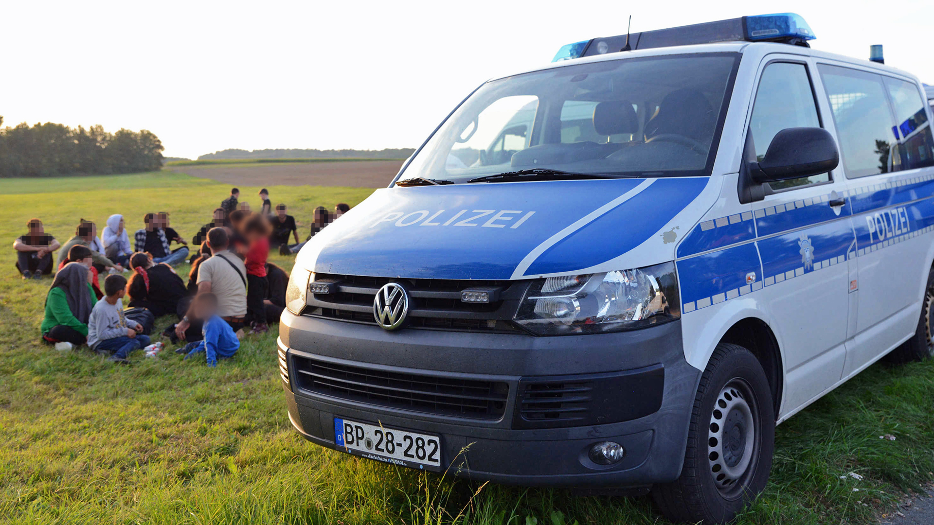 Eine Gruppe von Migranten aus Syrien und der Türkei sitzt neben einem Einsatzfahrzeug der Polizei in Sachsen (Foto: dpa/Baier)