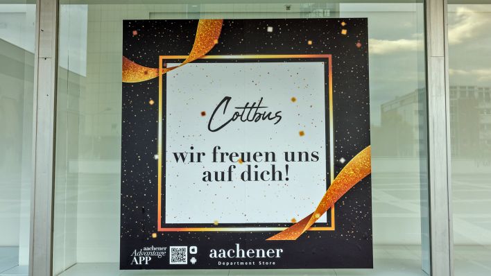 An einem Schaufenster des noch nicht eröffneten Modehauses "Aachener" hängt ein Imageplakat mit der Aufschrift "Cottbus, wir freuen uns auf dich!" (Foto: dpa/Hammerschmidt)