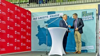 Der Lausitzbeauftragte Klaus Freytag übergibt dem Cottbuser Oberbürgermeister Tobias Schick auf einer Bühne den Scheck (Foto: rbb/Jahn)