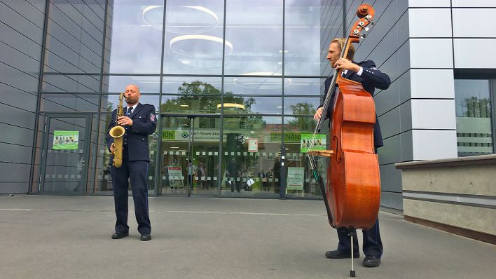 Zwei Musiker des Landespolizeiorchesters spielen vor dem Cottbuser Krankenhaus mit einem Kontrabass und einem Saxophon für Patienten.