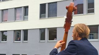 Ein Musiker des Landespolizeiorchesters spielt vor dem Cottbuser Krankenhaus für Patienten. Ein Patient mit Mundschutz schaut ihm vom Fenster aus zu.