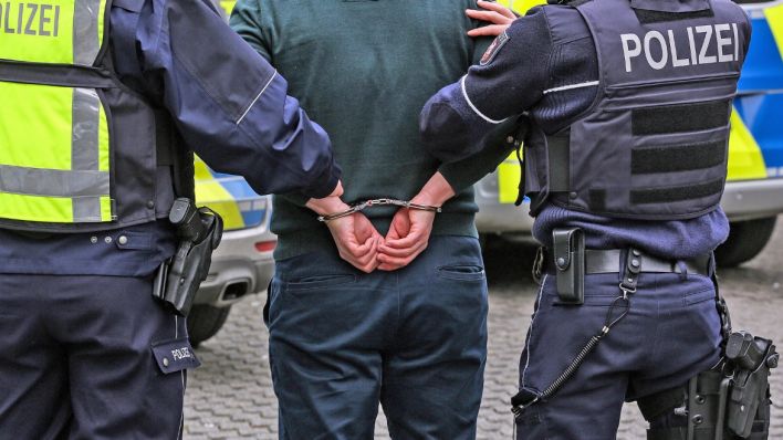 Zwei Polizisten mit einer Person mit Handschellen (Symbolfoto: imago/Traut)